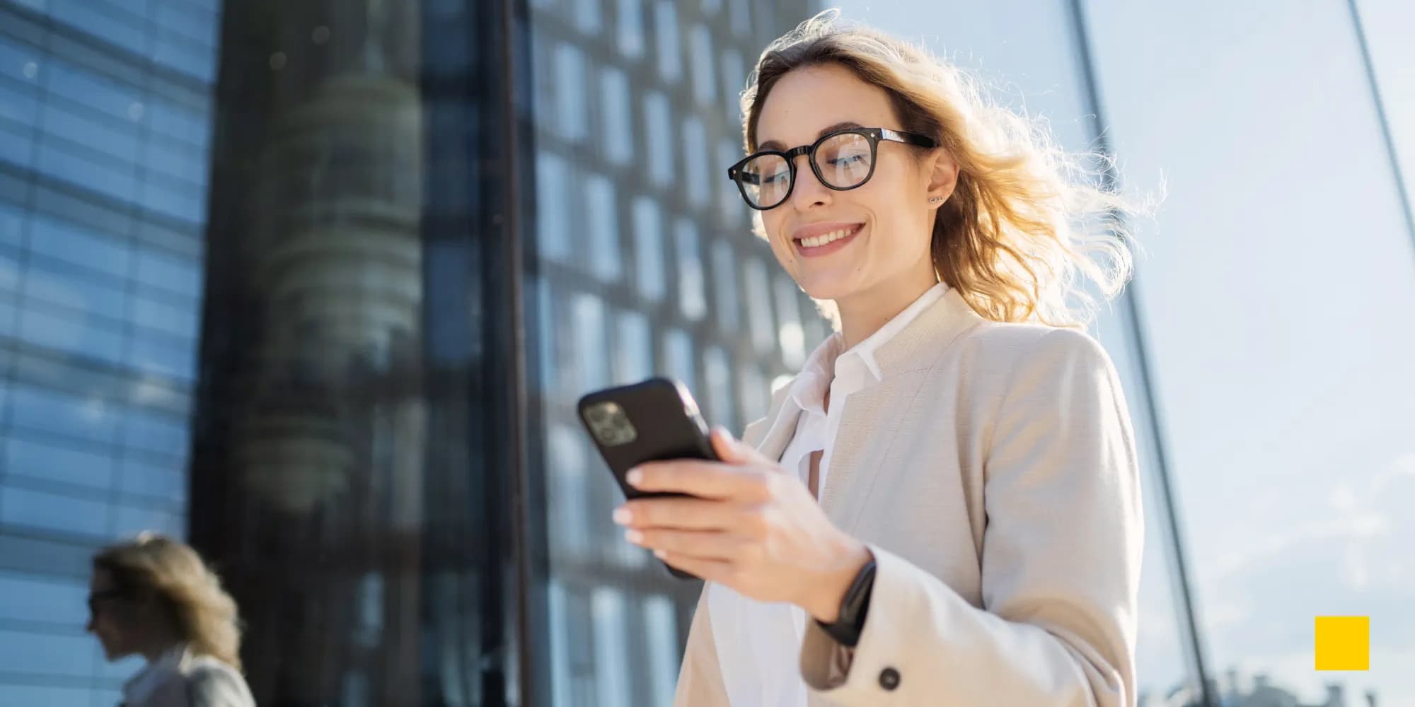 Profesional sonriendo mientras comparte una tarjeta de visita digital desde su smartphone frente a un edificio de oficinas